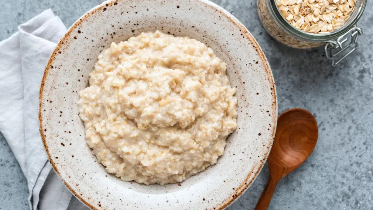 Cremiger Haferbrei im Teller, daneben ein Glas Haferflocken und ein Holzlöffel. Perfekt für ein einfaches Porridge Rezept.