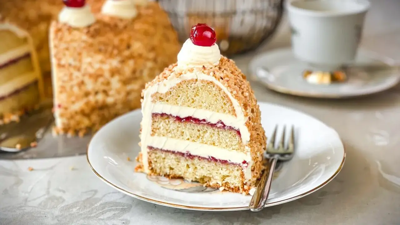 Ein Stück Frankfurter Kranz mit Buttercreme und Kirschen, umhüllt von gehackten Nüssen. Ein Genuss für jeden Kaffeetisch.
