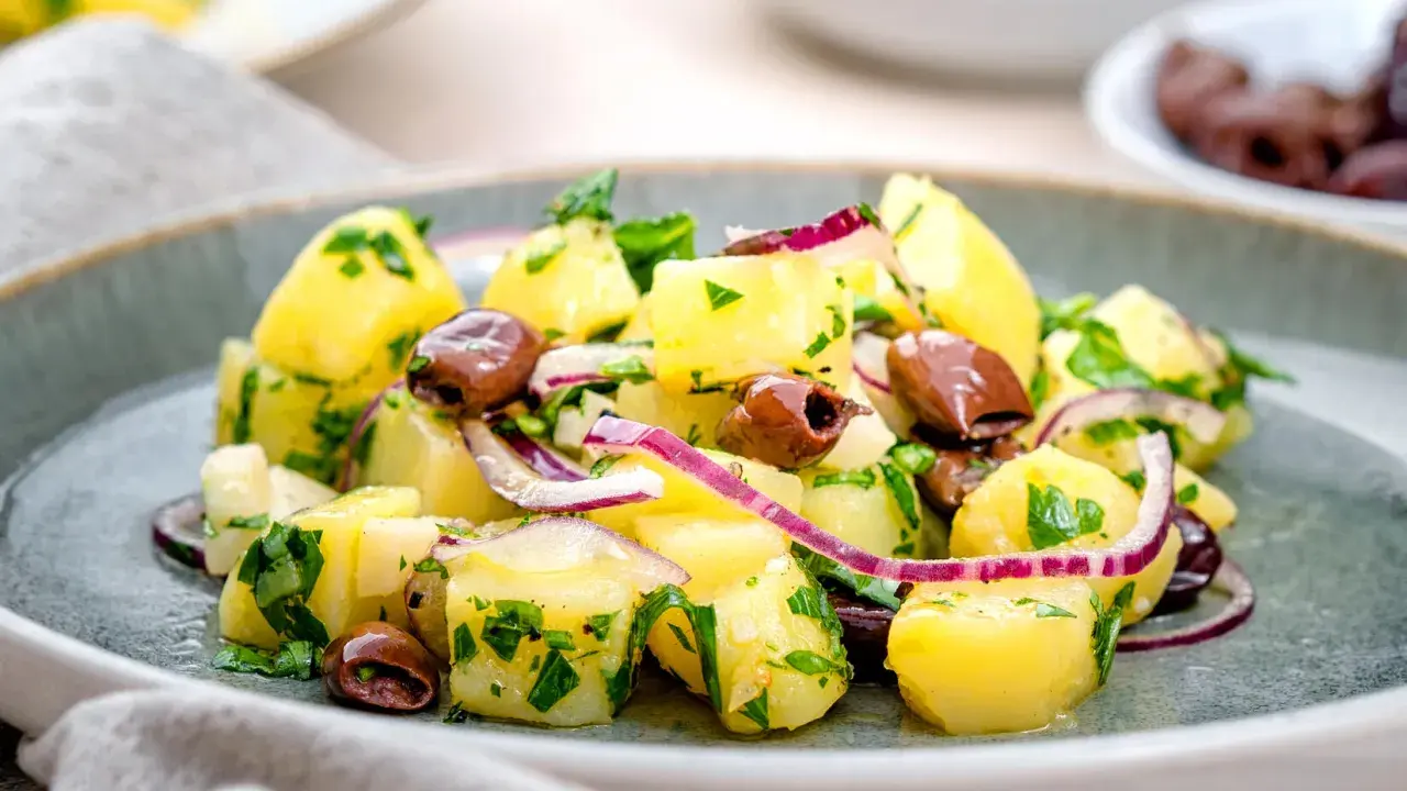 Ein köstlicher italienischer Kartoffelsalat mit Oliven, roten Zwiebeln und frischer Petersilie auf einem grauen Teller.