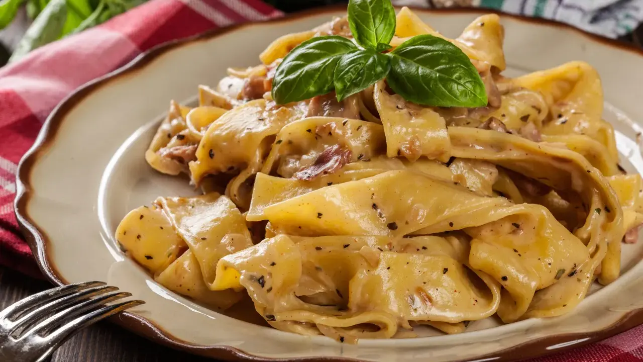 Breite, cremige Pappardelle-Nudeln mit Speck und Kräutern, garniert mit Basilikum.