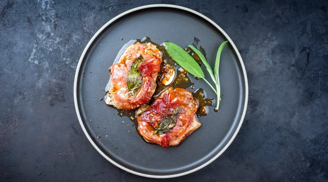 Zwei in Prosciutto eingewickelte Fleischstücke mit Salbei, glasiert und auf einem Teller serviert. Ein köstliches Beispiel für italienische Gerichte.