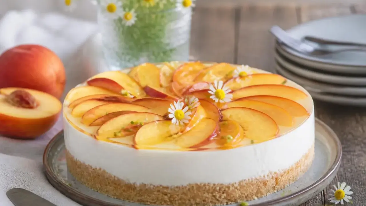Ein köstlicher Kuchen ohne Backen, belegt mit frischen Pfirsichscheiben und kleinen Gänseblümchen.