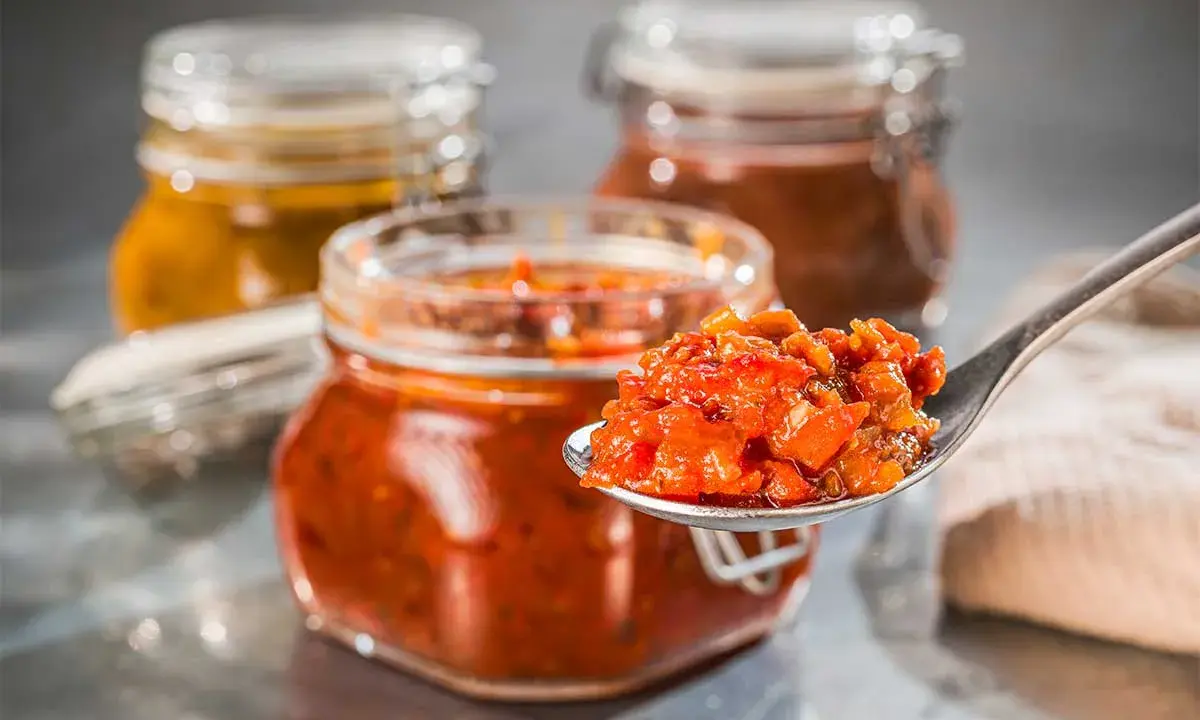 Ein Löffel voll leckerem Tomaten-Chutney, perfekt für Ihr nächstes Tomaten-Chutney-Rezept. Im Hintergrund stehen weitere Gläser mit Chutney.