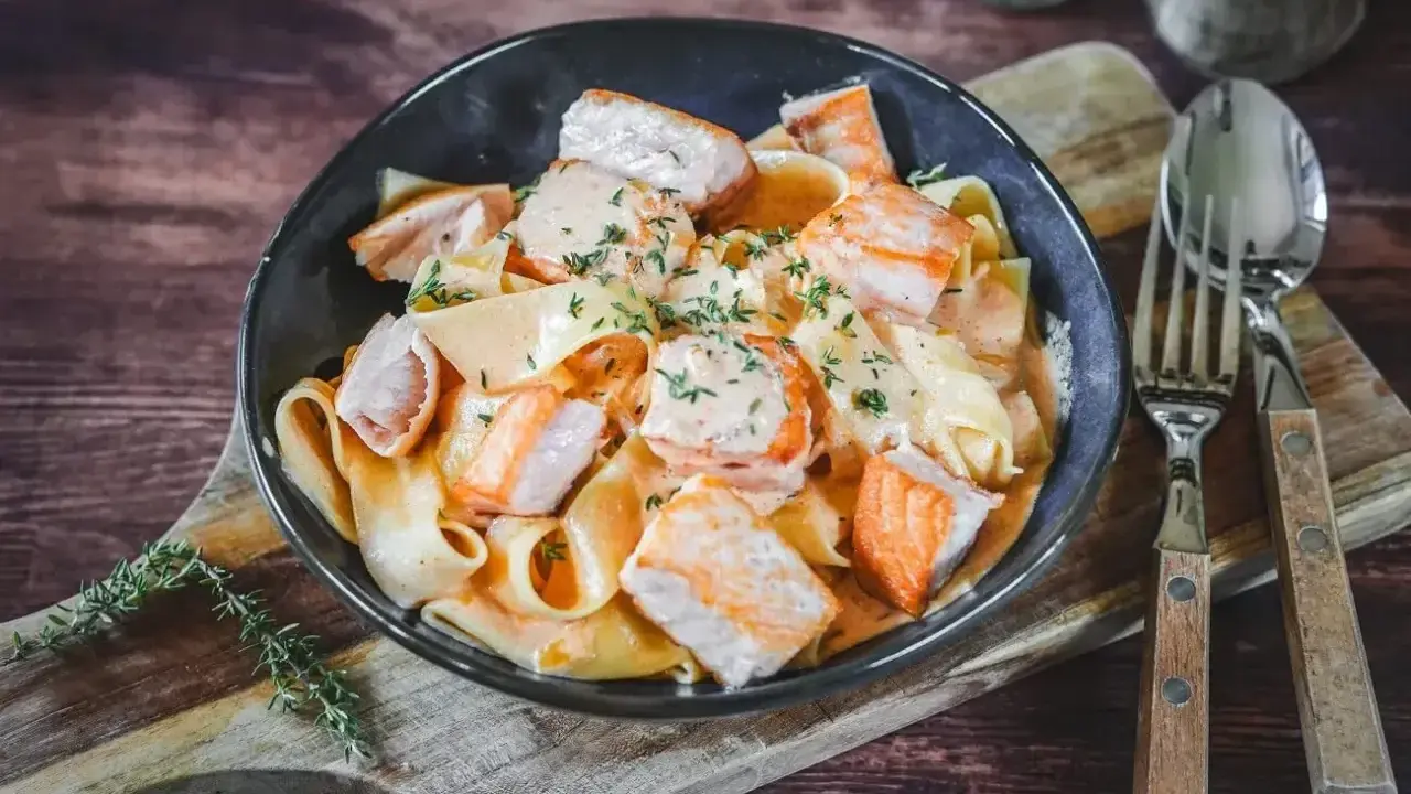 Breite Bandnudeln mit saftigen Lachs-Stücken in cremiger Lachs Sahne Sauce, garniert mit frischen Kräutern. Ein Genuss!