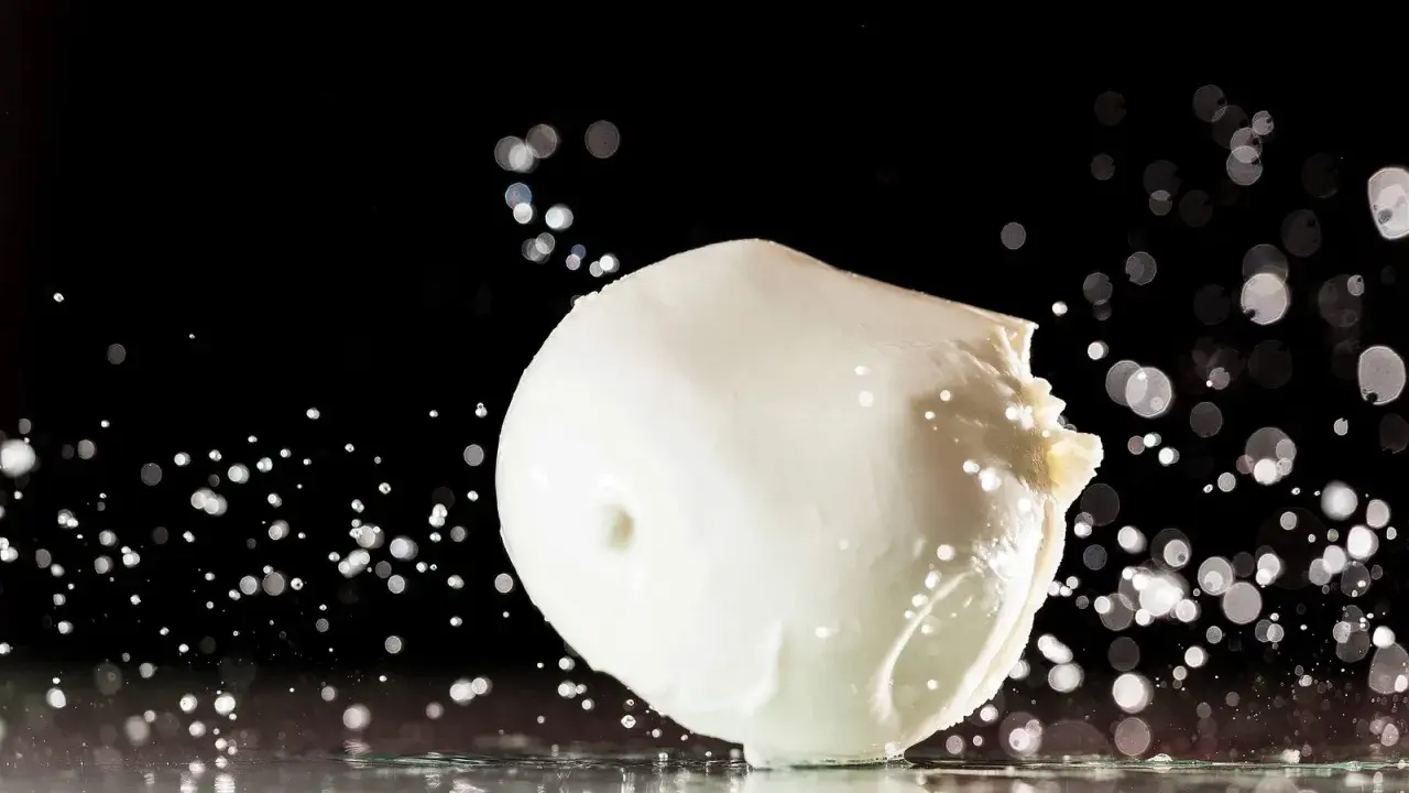 Ein frischer Fior di Latte, der auf einer spiegelnden Oberfläche liegt, umgeben von Wassertropfen und Bokeh-Lichtern.