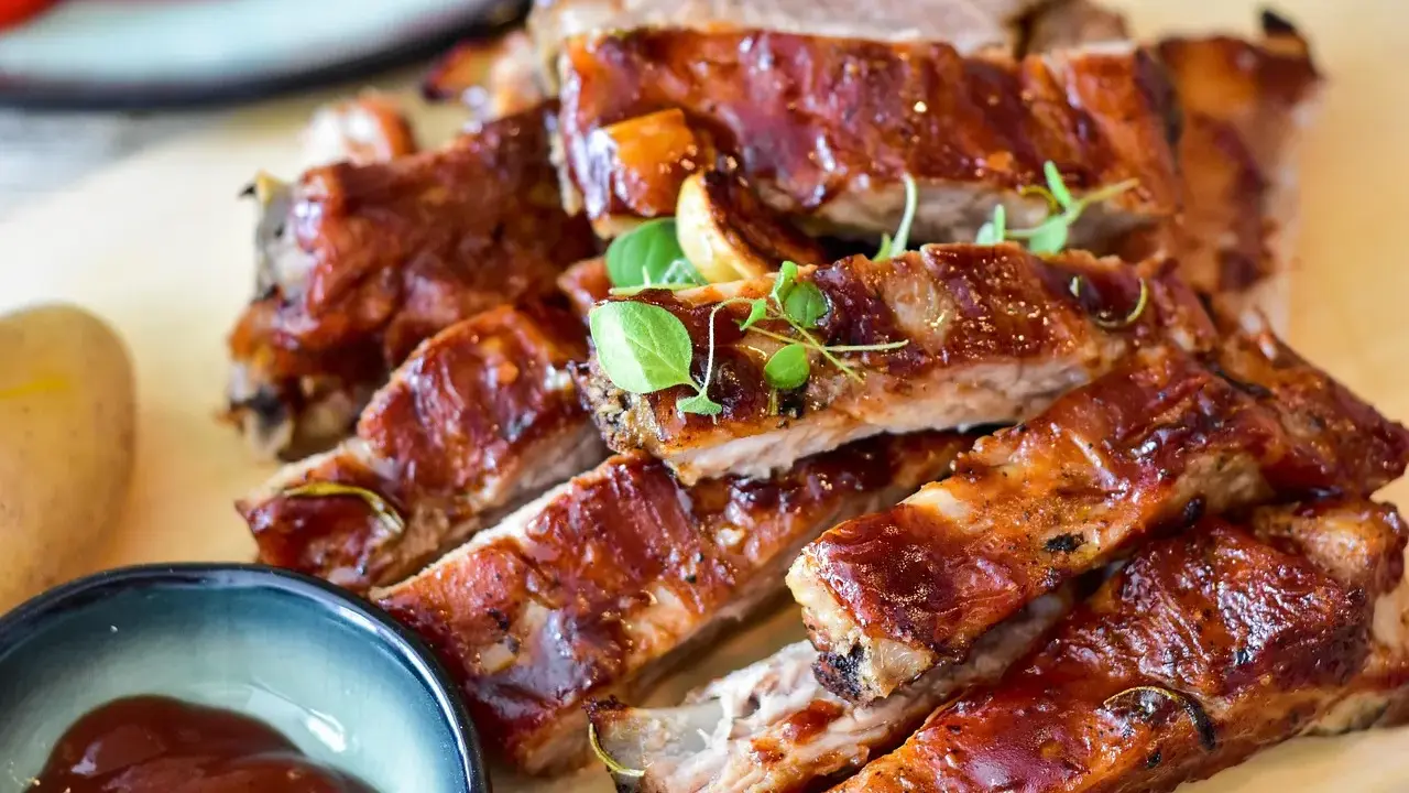 Saftige Spareribs mit glänzender Marinade, garniert mit frischen Kräutern. Dazu eine Schale BBQ-Sauce und eine Kartoffel.