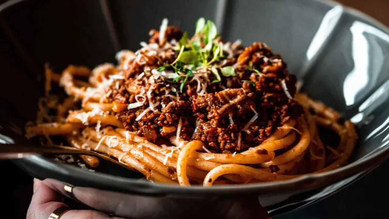 Eine Schüssel mit herzhaftem Pasta al Ragu, garniert mit frischen Kräutern und geriebenem Käse.