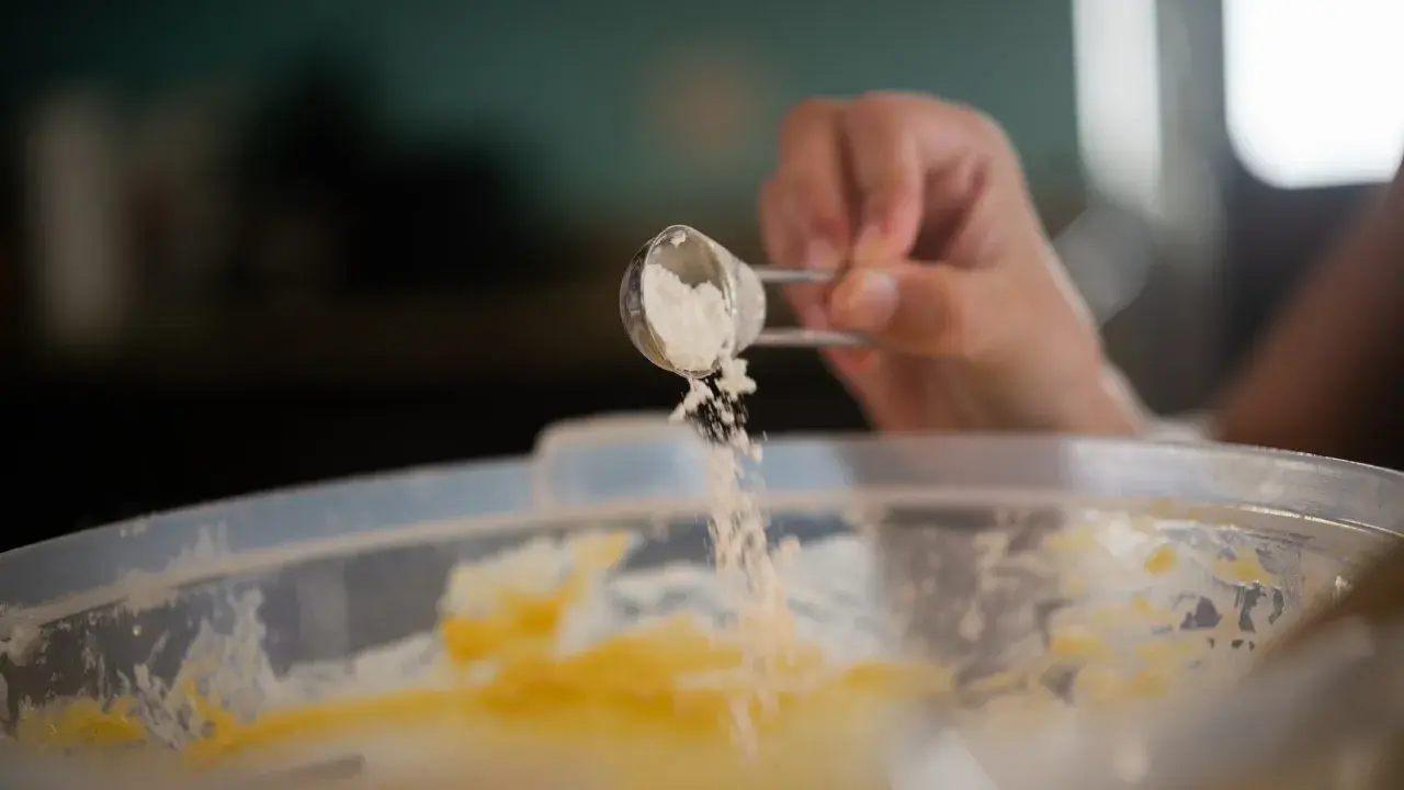 Eine Hand streut Natron aus einem Löffel in eine Schüssel mit Teig. Perfekt für das Backen!