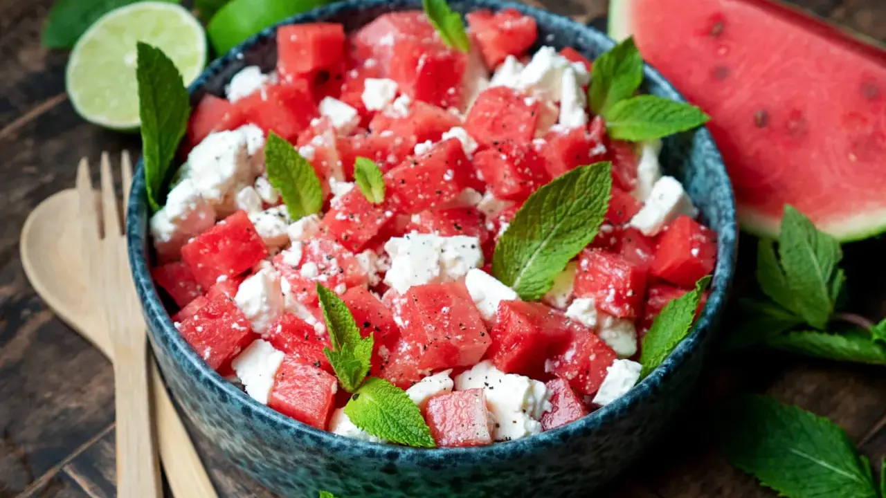 Erfrischender Wassermelonensalat mit Feta und Minze, perfekt für ein leichtes sommersalat rezept. Dazu passen Limettenspalten und Holzbesteck.
