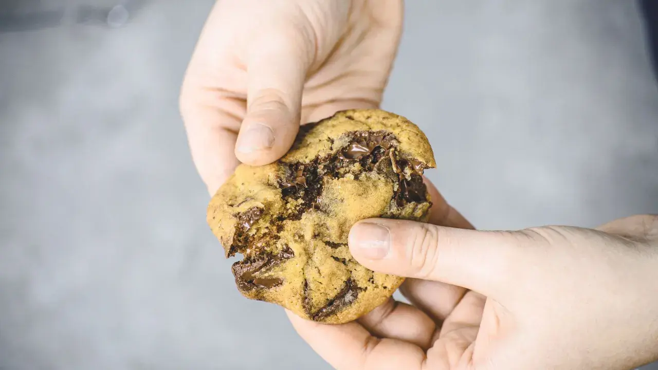Hände halten einen weichen Chocolate Chip Cookie, der gerade zerbrochen wurde. Das Innere ist voller geschmolzener Schokolade. Ein perfektes Cookies Rezept weich.