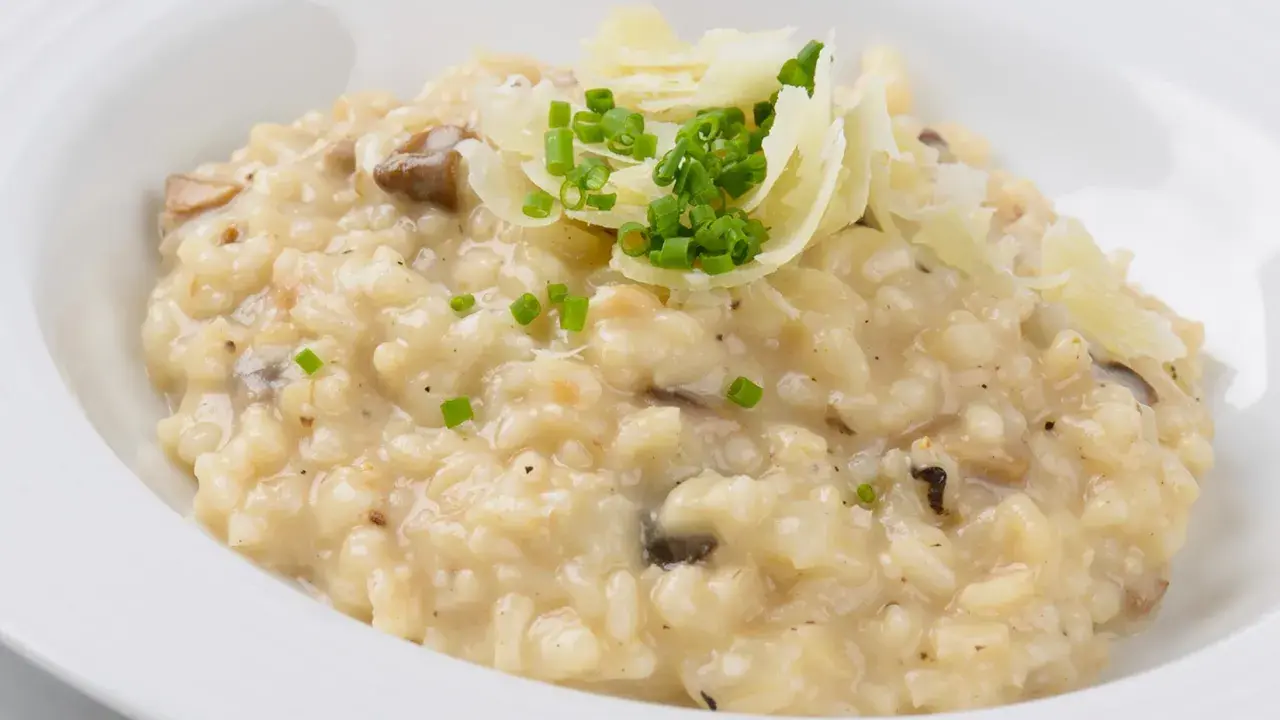 Cremiger Pilz-Risotto-Reis, garniert mit Parmesan und Schnittlauch, serviert in einer weißen Schüssel.