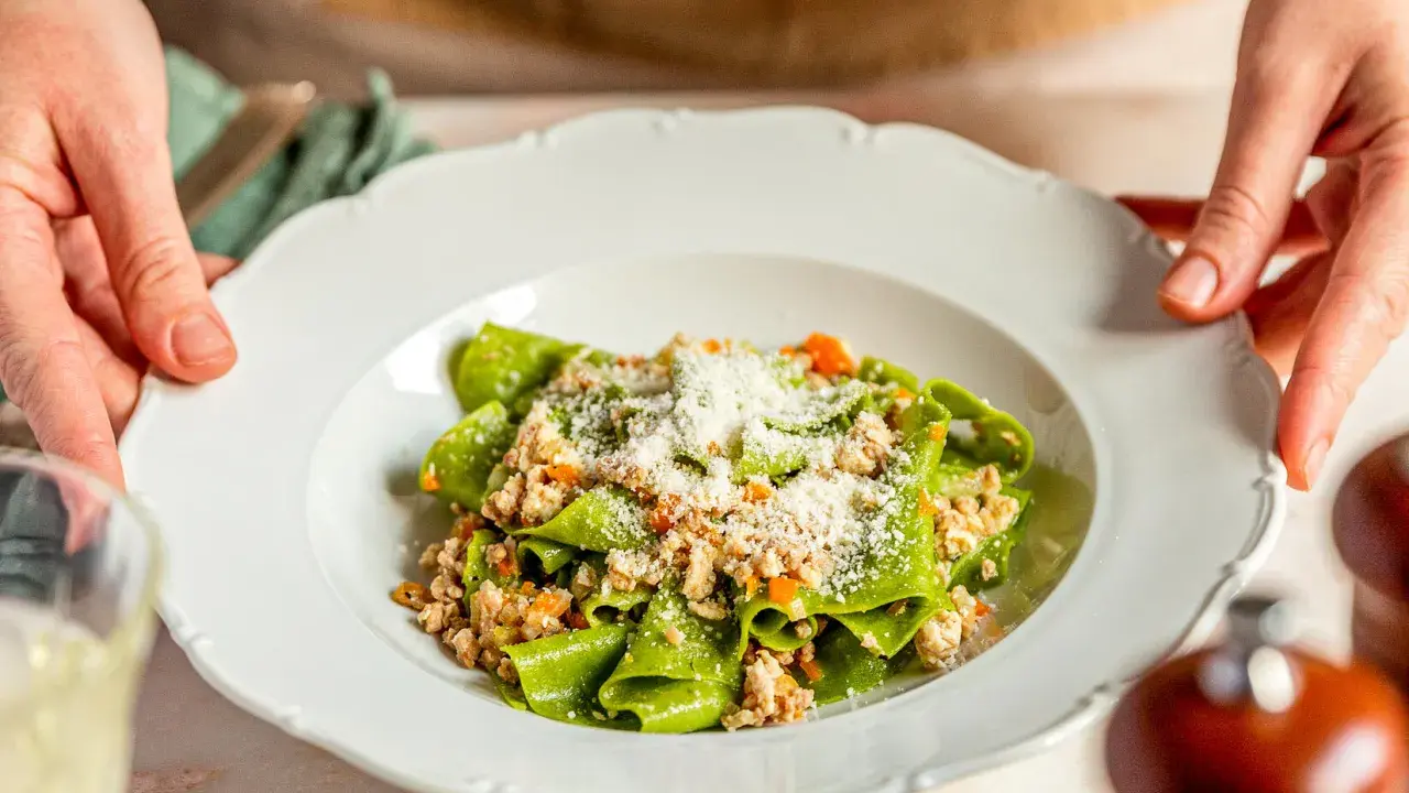 Grüne Bandnudeln mit herzhaftem ragu bianco und Parmesan bestreut, serviert auf einem weißen Teller.