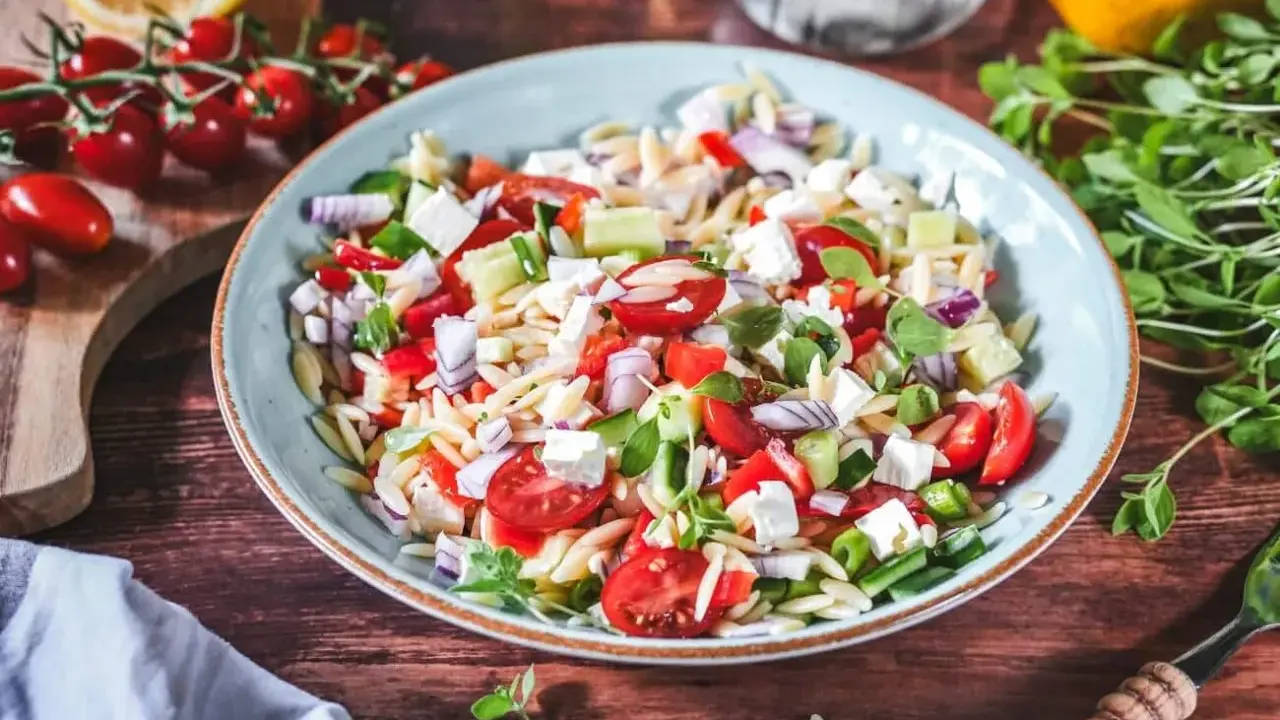 Frischer Kritharaki Salat mit Tomaten, Gurken, Feta und roten Zwiebeln, garniert mit Kräutern. Ein leichter Genuss!