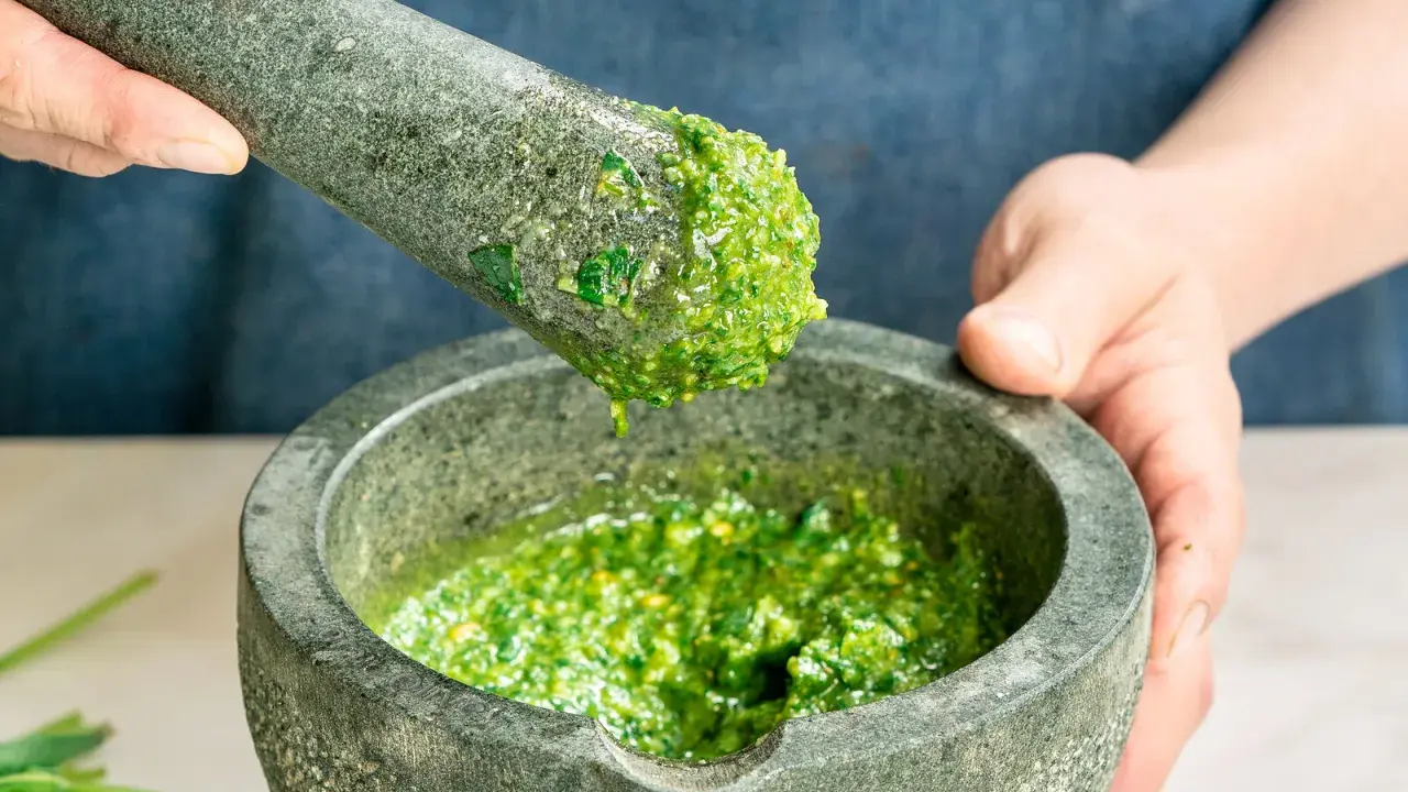 Frische Kräuter werden im Mörser zu einem leuchtend grünen pesto genovese zermahlen.