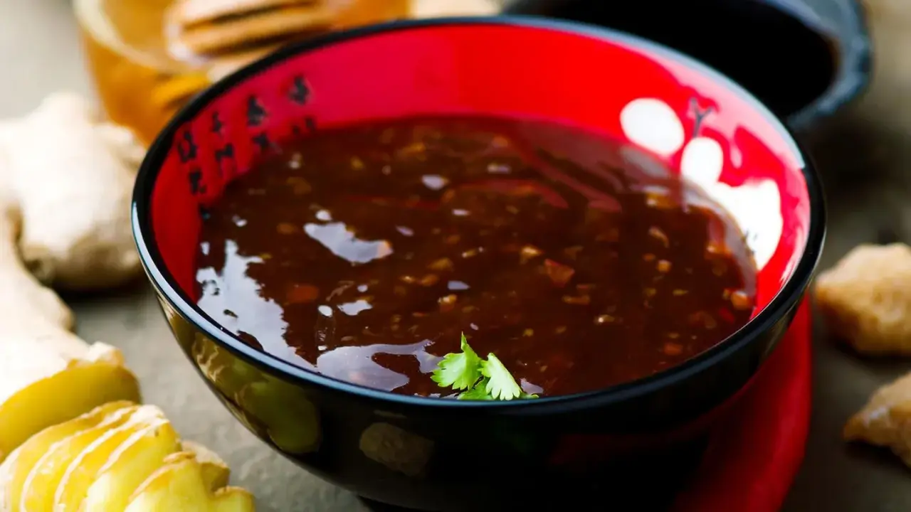 Schwarze Schüssel mit glänzender Teriyaki-Sauce, umgeben von Ingwer, Chili und Honig. Perfekt für dein Teriyaki Sauce Rezept!