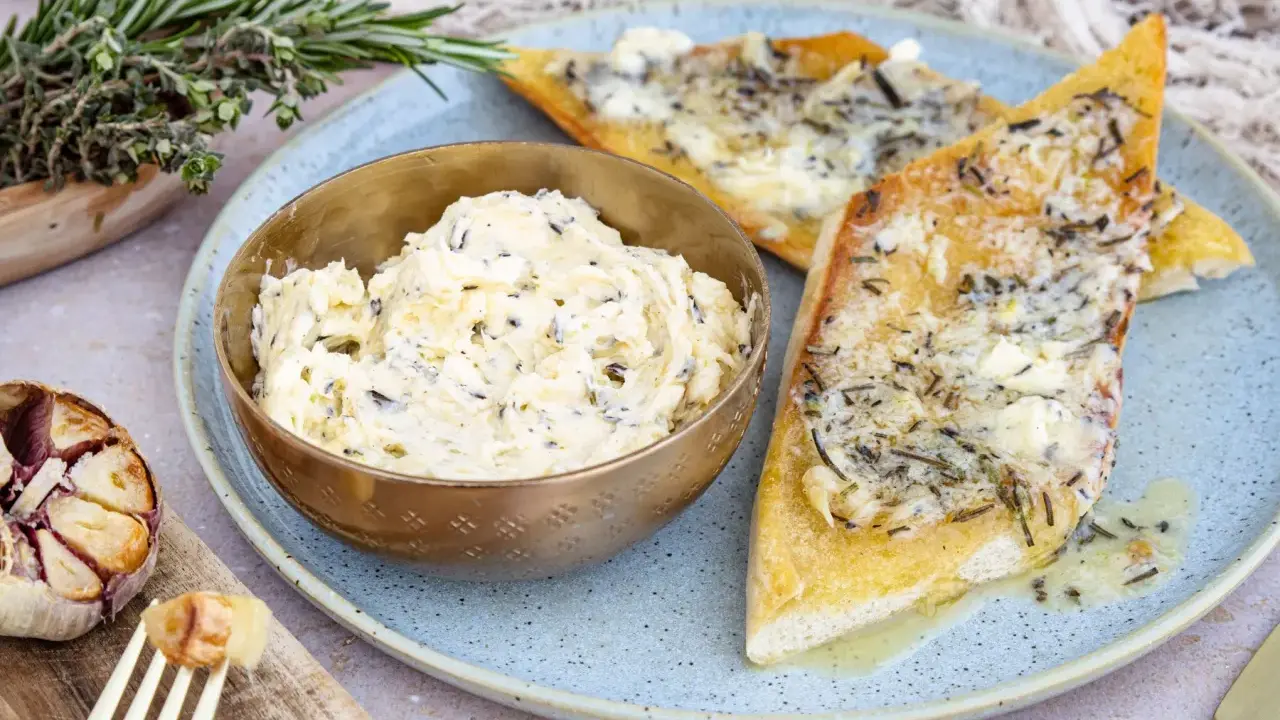 Schüssel mit selbstgemachter Knoblauchbutter, daneben gerösteter Knoblauch und Kräuterbrot. Perfekt zum **knoblauchbutter selber machen**.