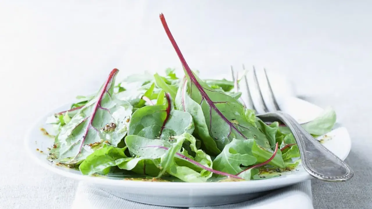 Frischer mangold salat mit roten Stielen, beträufelt mit Dressing, auf einem Teller mit einer Gabel.
