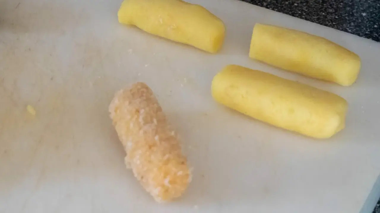 Vier Kartoffelstäbchen liegen auf einem Schneidebrett. Eines ist bereits paniert, die anderen drei warten darauf, dass sie **kroketten selber machen** können.