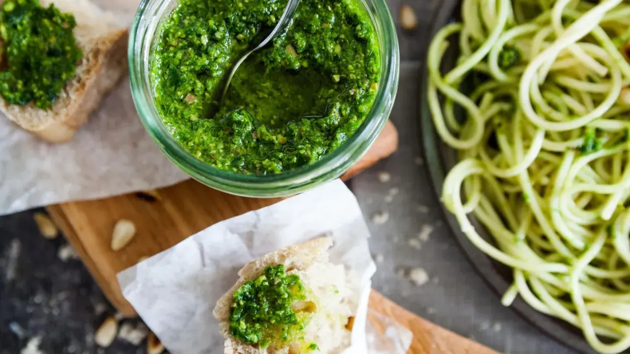 Frisches Basilikumpesto rezept in einem Glas, daneben Brot mit Pesto und eine Portion Spaghetti. Perfekt für ein schnelles Mittagessen.