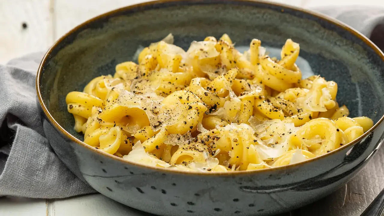 Eine Schüssel mit italienischen Nudeln, bestreut mit Parmesan und schwarzem Pfeffer, serviert auf einem rustikalen Tisch.