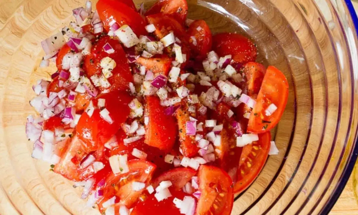 Frischer Tomatensalat mit roten Zwiebeln und Kräutern, bereit für Feta.