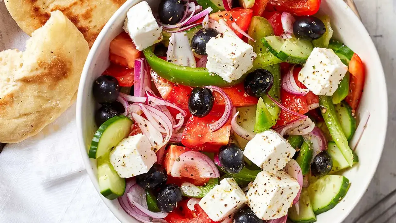 Frischer griechischer Salat mit Tomaten, Gurken, roten Zwiebeln, Oliven und Feta-Käse, serviert mit Fladenbrot.