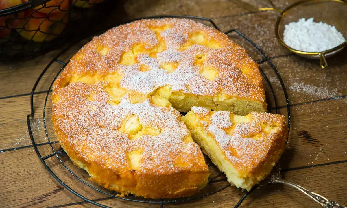Ein saftiger, versunkener Apfelkuchen nach Omas Rezept, bestäubt mit Puderzucker. Ein Stück wurde bereits herausgenommen.