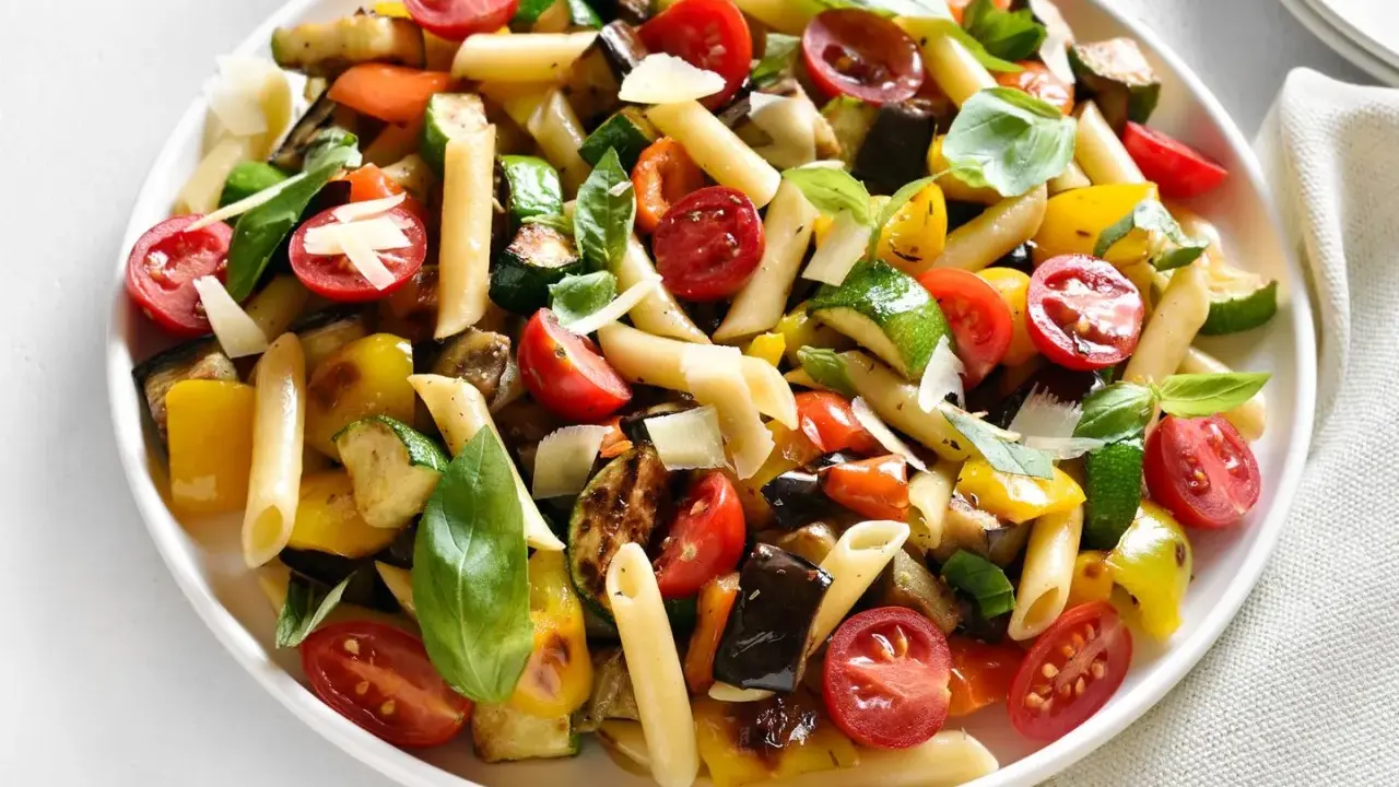 Bunter Nudelsalat ohne Mayo mit Penne, gegrilltem Gemüse wie Zucchini, Aubergine, Paprika und Kirschtomaten, garniert mit Basilikum und Parmesan.