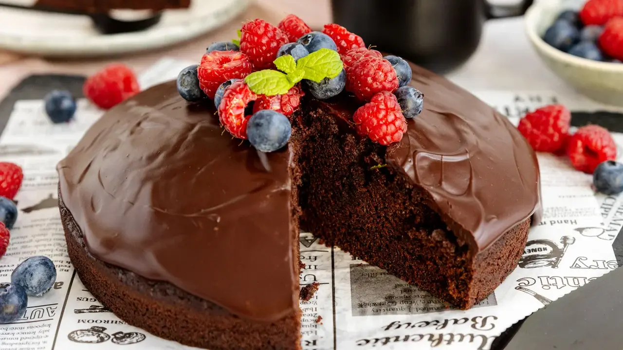 Ein saftiger veganer Schokokuchen mit glänzender Schokoladenglasur, garniert mit frischen Himbeeren und Blaubeeren.