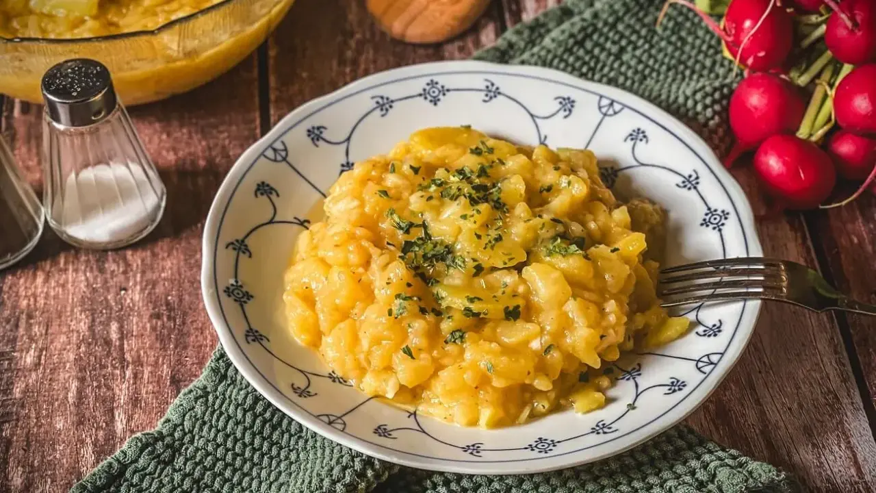 Ein Teller mit Omas Kartoffelsalat, garniert mit Petersilie. Daneben ein Glas mit Radieschen und Gewürzstreuer.