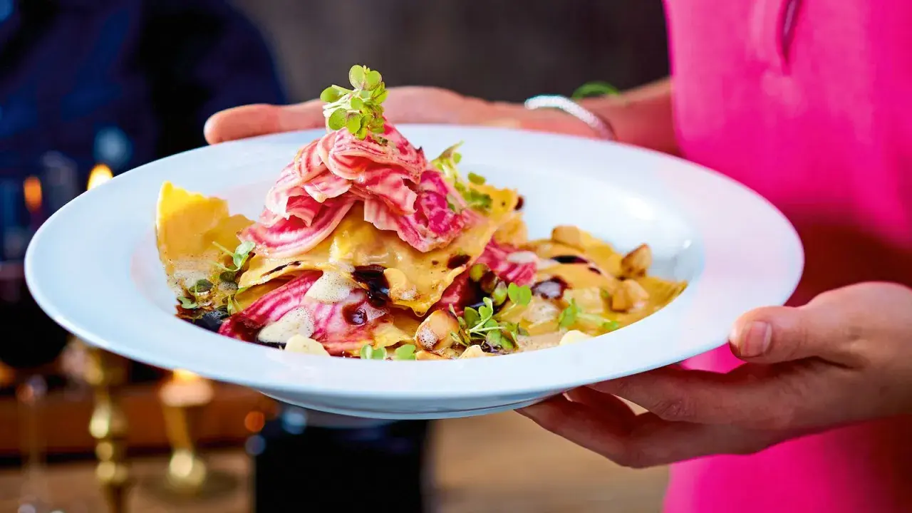 Ein Teller mit Ravioli, garniert mit Streifen von roter Bete und Kräutern. Ein Gericht, das perfekt für "Das perfekte Dinner Rezepte" wäre.