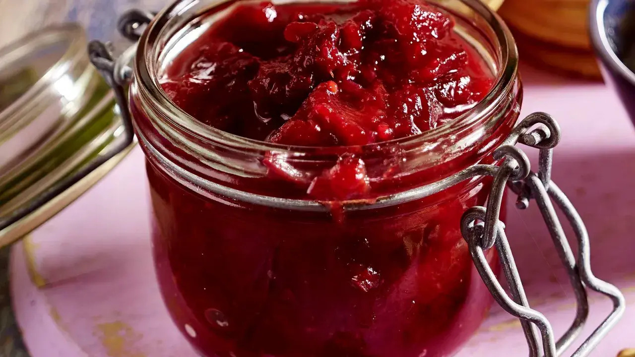 Ein Glas mit leuchtend rotem Zwetschgen-Chutney, bereit, zu Käse oder Gebäck serviert zu werden.