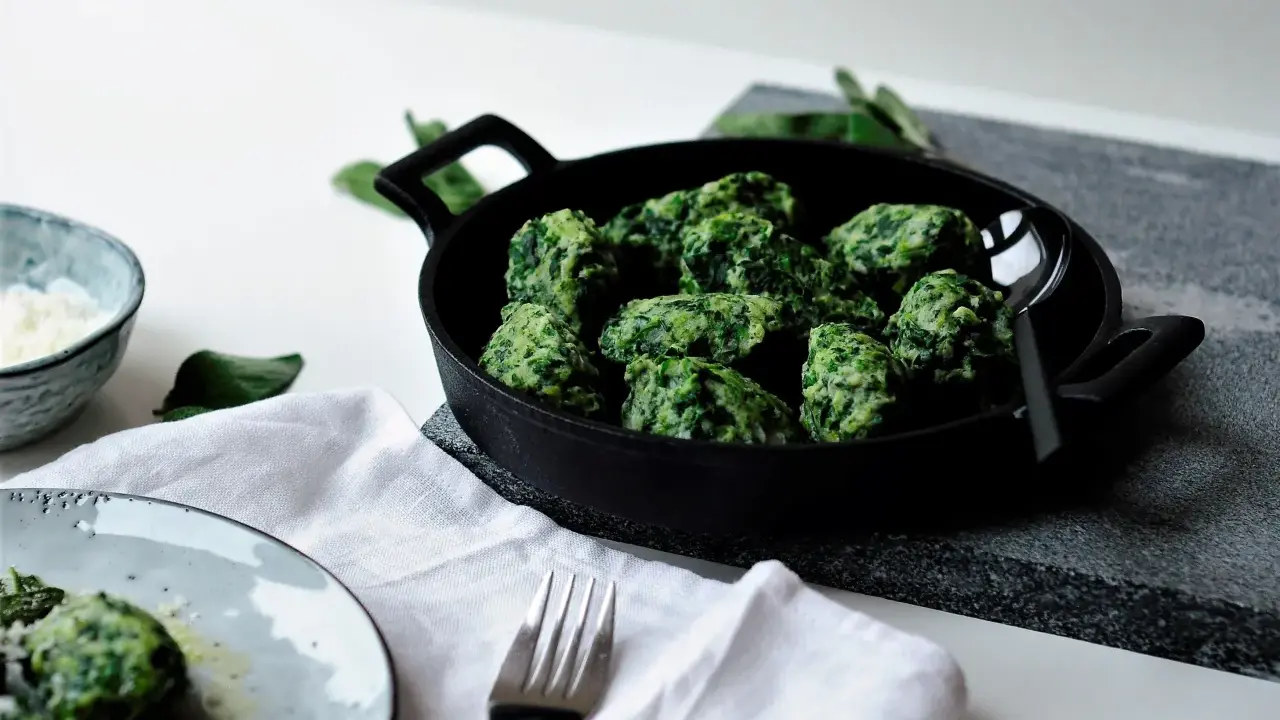 Grüne Malfatti, zubereitet nach einem einfachen Rezept, serviert in einer Gusseisenpfanne. Daneben ein Schälchen mit geriebenem Käse und ein Teller mit den fertigen Malfatti.