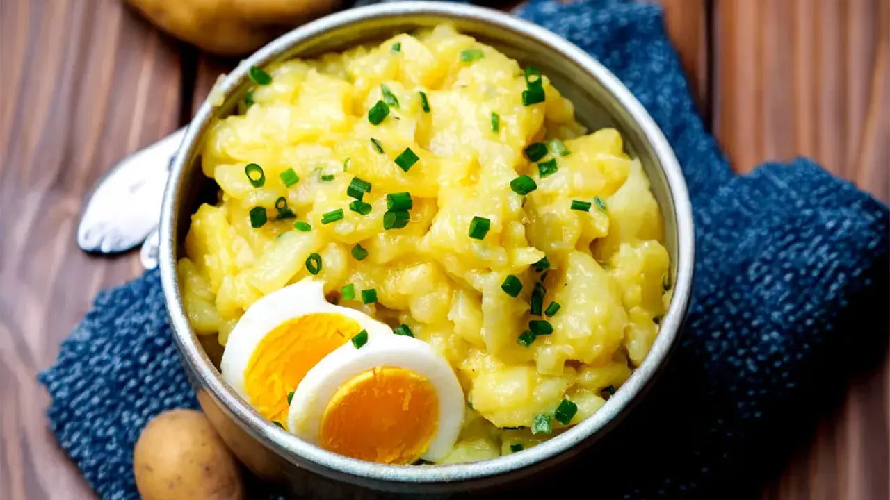 Schüssel mit warmem Kartoffelsalat, garniert mit Schnittlauch und Ei. Ein herzhaftes Gericht, das zum Genießen einlädt.