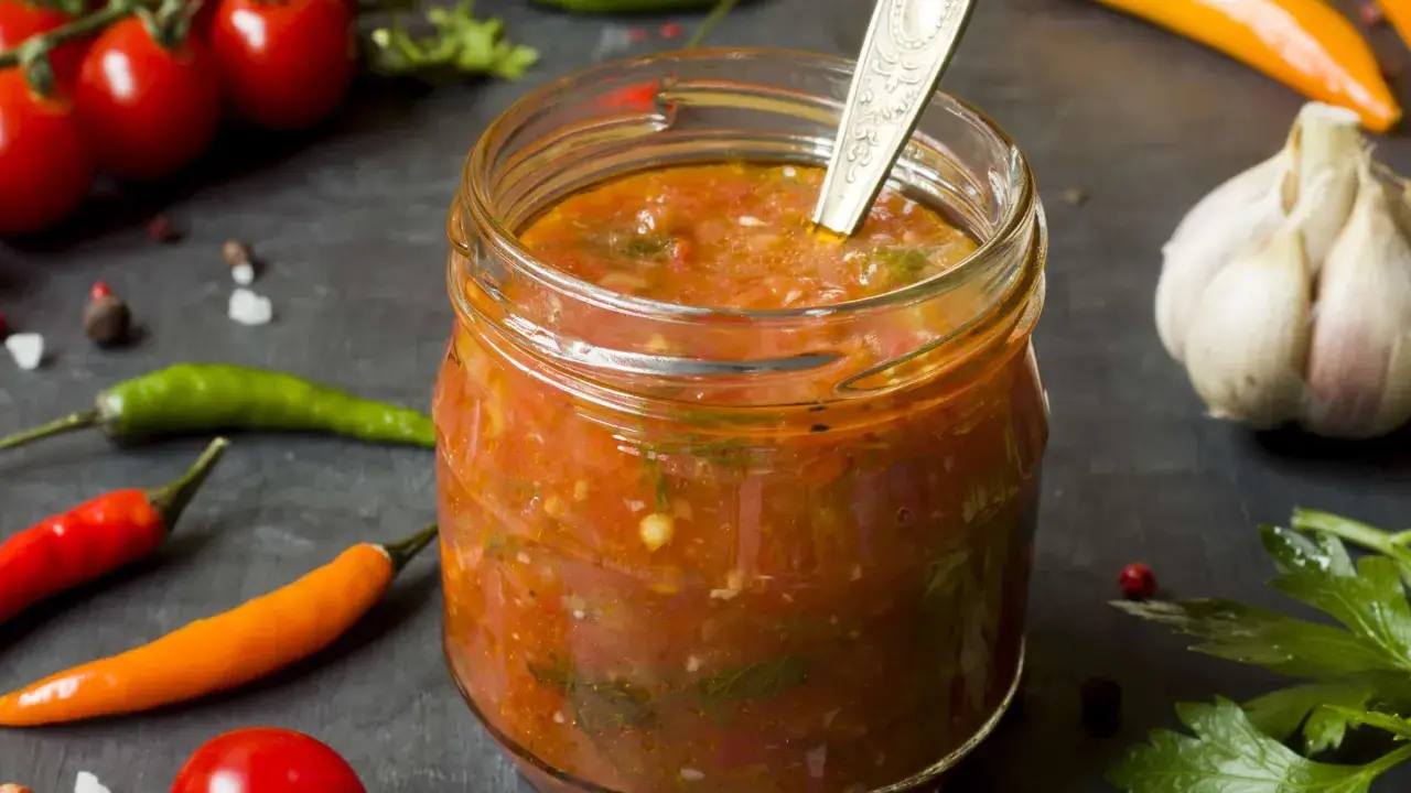 Ein Glas mit würzigem Zucchini-Ketchup, umgeben von frischen Tomaten, Chilis und Knoblauch.
