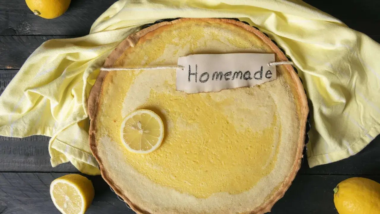 Ein frisch gebackener Joghurt Zitronen Kuchen mit einer Zitronenscheibe und dem Schriftzug "Homemade" auf einem gelben Tuch.