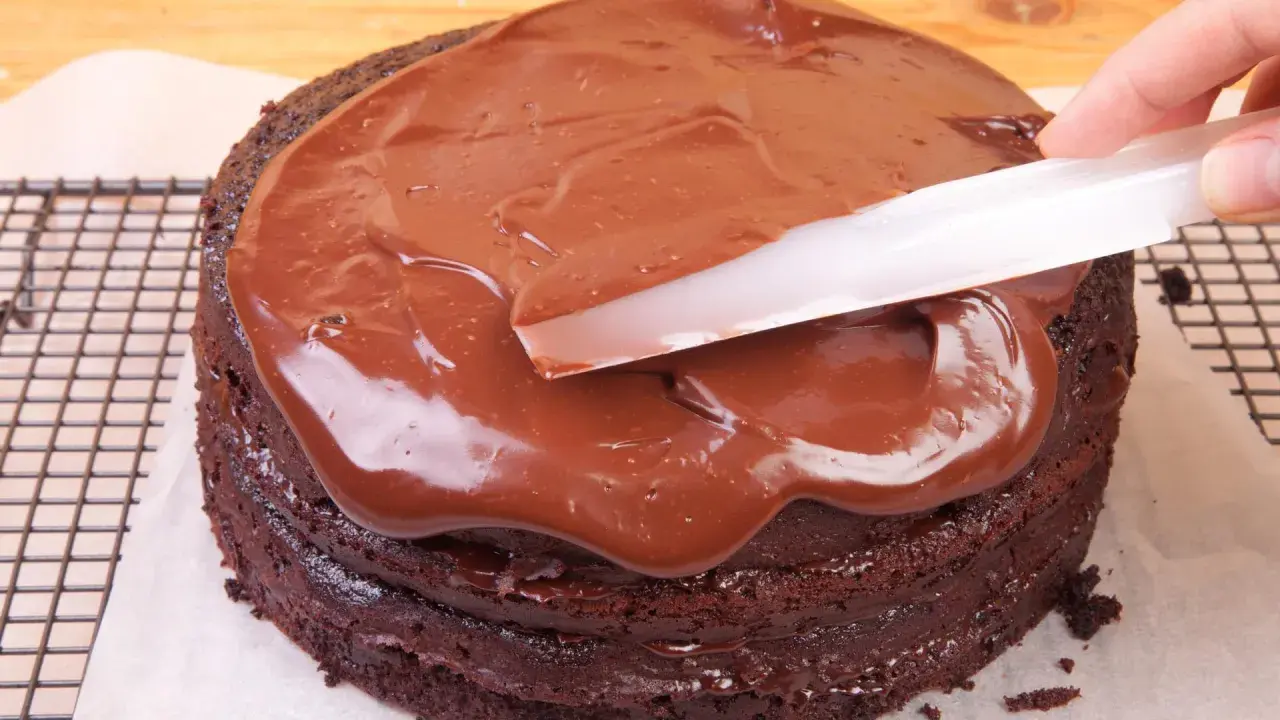 Schokoladenkuchen wird mit glatter, glänzender Ganache überzogen. Was ist eine Ganache? Eine köstliche Mischung aus Schokolade und Sahne.