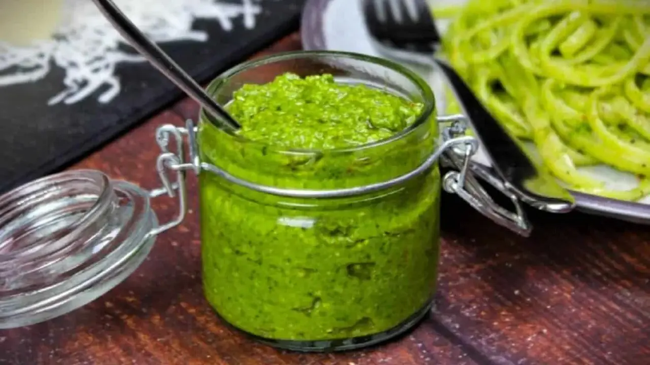 Frisches Rucola Pesto in einem Glas mit Löffel, daneben eine Portion Pasta.