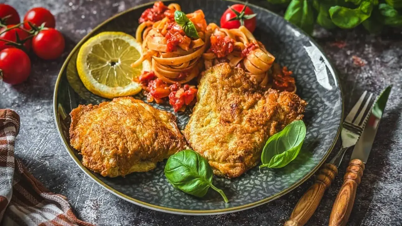 Piccata Milanese mit Pasta und frischen Tomaten, garniert mit Basilikum und Zitrone. Ein köstliches Gericht, das Appetit macht.