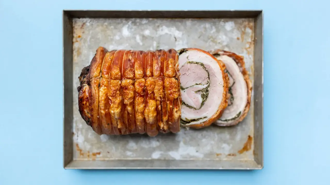 Ein knusprig gebratenes Stück Porchetta, ein italienisches Schweinebraten-Gericht, liegt auf einem Blech.
