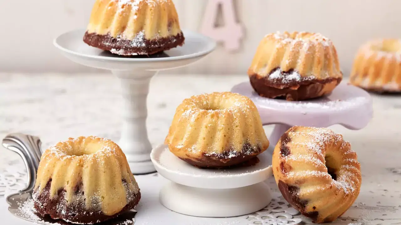Mehrere kleine, mit Puderzucker bestäubte Mini Gugelhupf-Kuchen mit Schokoladenboden stehen auf verschiedenen Etageren.