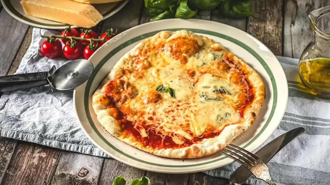 Eine köstliche Pizza Quattro Formaggi mit vier Käsesorten, serviert mit frischen Tomaten und Basilikum auf einem Holztisch.