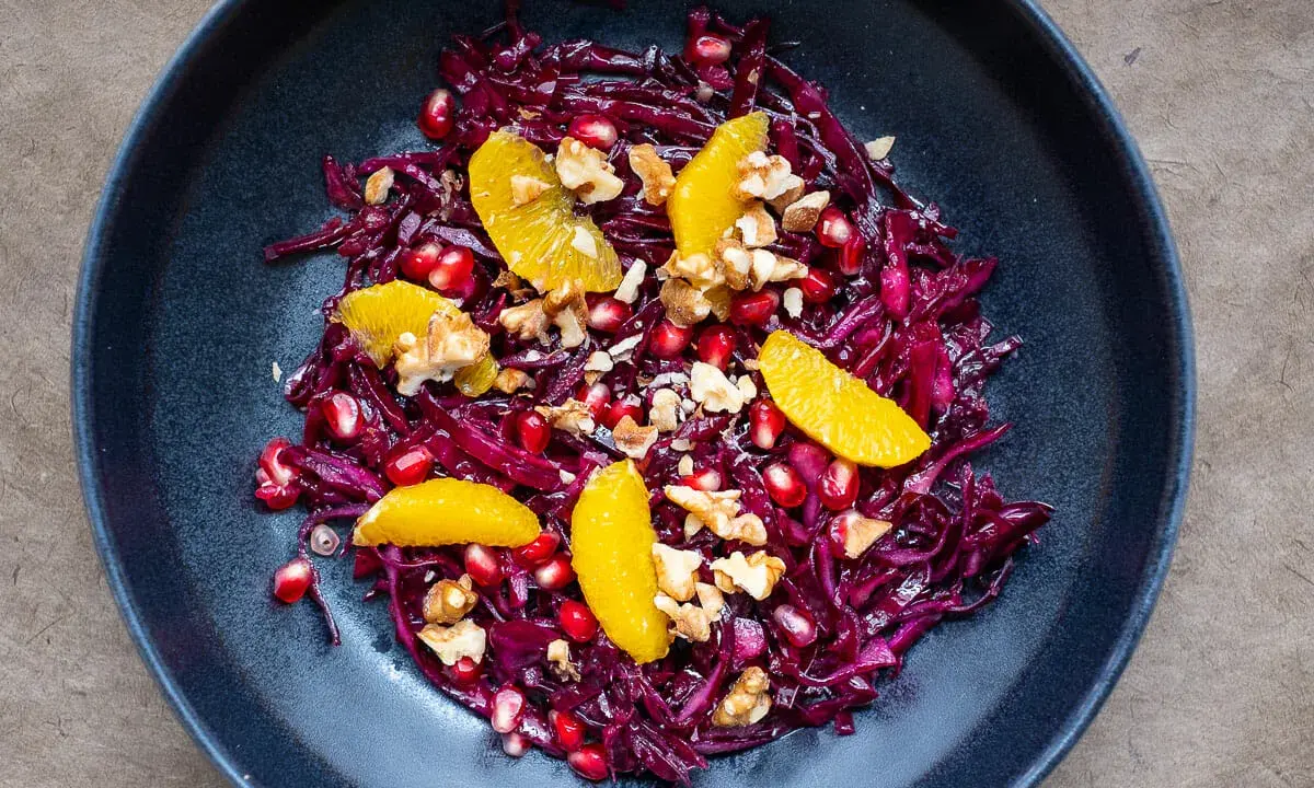 Ein bunter rotkohl salat mit Orangenfilets, Granatapfelkernen und Walnüssen in einer dunklen Schüssel.