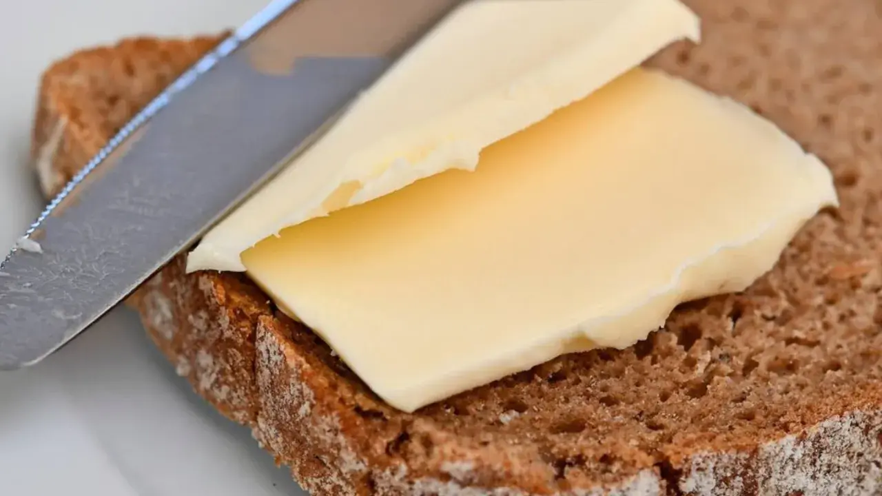 Ein Messer verteilt cremige Butter oder Margarine auf einer Scheibe dunklem Brot.
