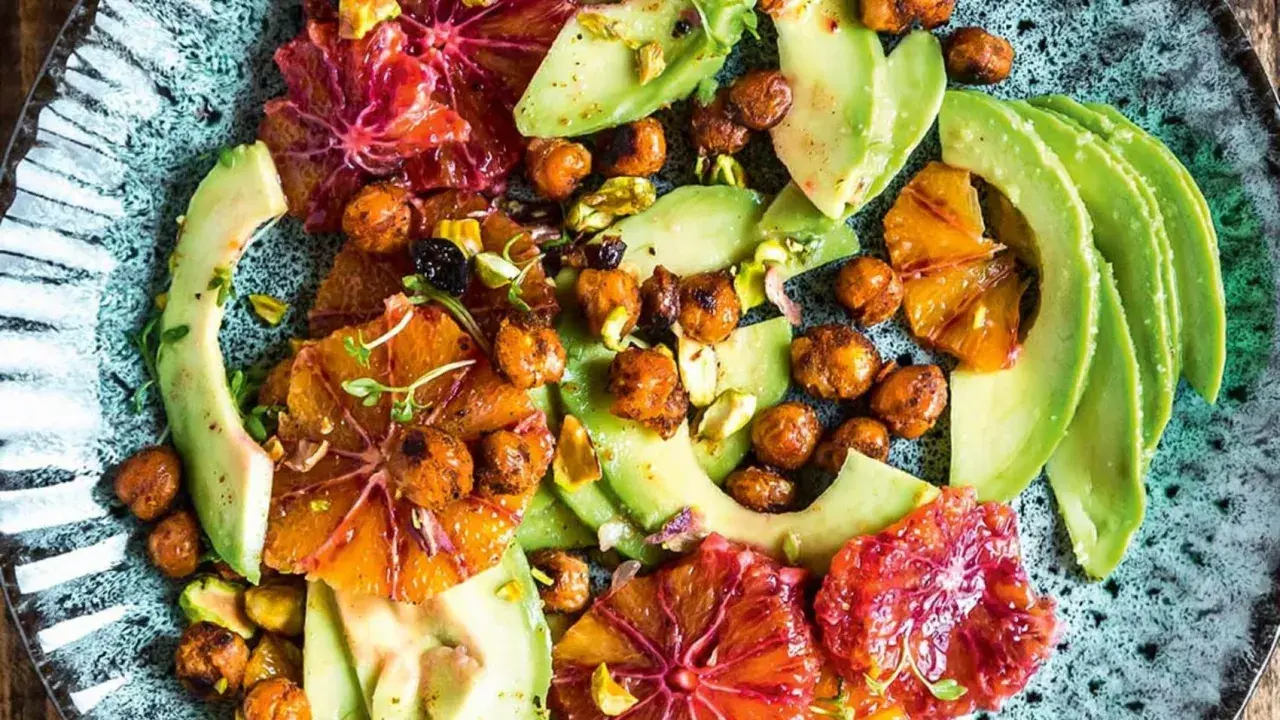 Ein bunter Avocado-Salat mit Blutorangen, Kichererbsen und Pistazien auf einem rustikalen Teller.