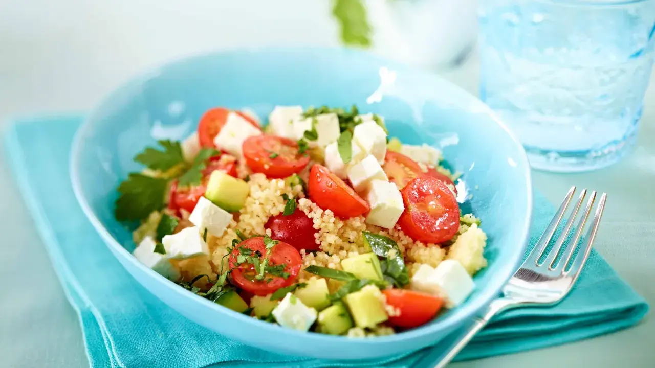 Erfrischender Couscous Salat mit Feta, Tomaten und Gurke in einer blauen Schüssel, bereit zum Genießen.