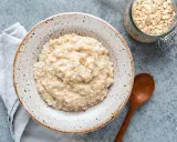Cremiger Haferbrei im Teller, daneben ein Glas Haferflocken und ein Holzlöffel. Perfekt für ein einfaches Porridge Rezept.