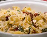Farfalle-Nudelsalat mit getrockneten Tomaten, Feta und Pinienkernen, garniert mit frischen Kräutern. Ein köstliches Gericht.