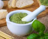 Frisches Pesto im Mörser, bereit für ein köstliches Rezept. Daneben liegen Brot, Parmesan, Knoblauch und Basilikum.