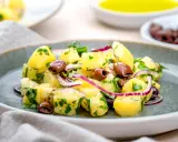 Ein köstlicher italienischer Kartoffelsalat mit Oliven, roten Zwiebeln und frischer Petersilie auf einem grauen Teller.